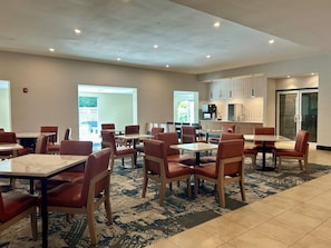 A hotel dining area with multiple tables and chairs, a kitchen area, and a view of the outdoors. - La Quinta Inn & Suites by Wyndham Danbury (Danbury)