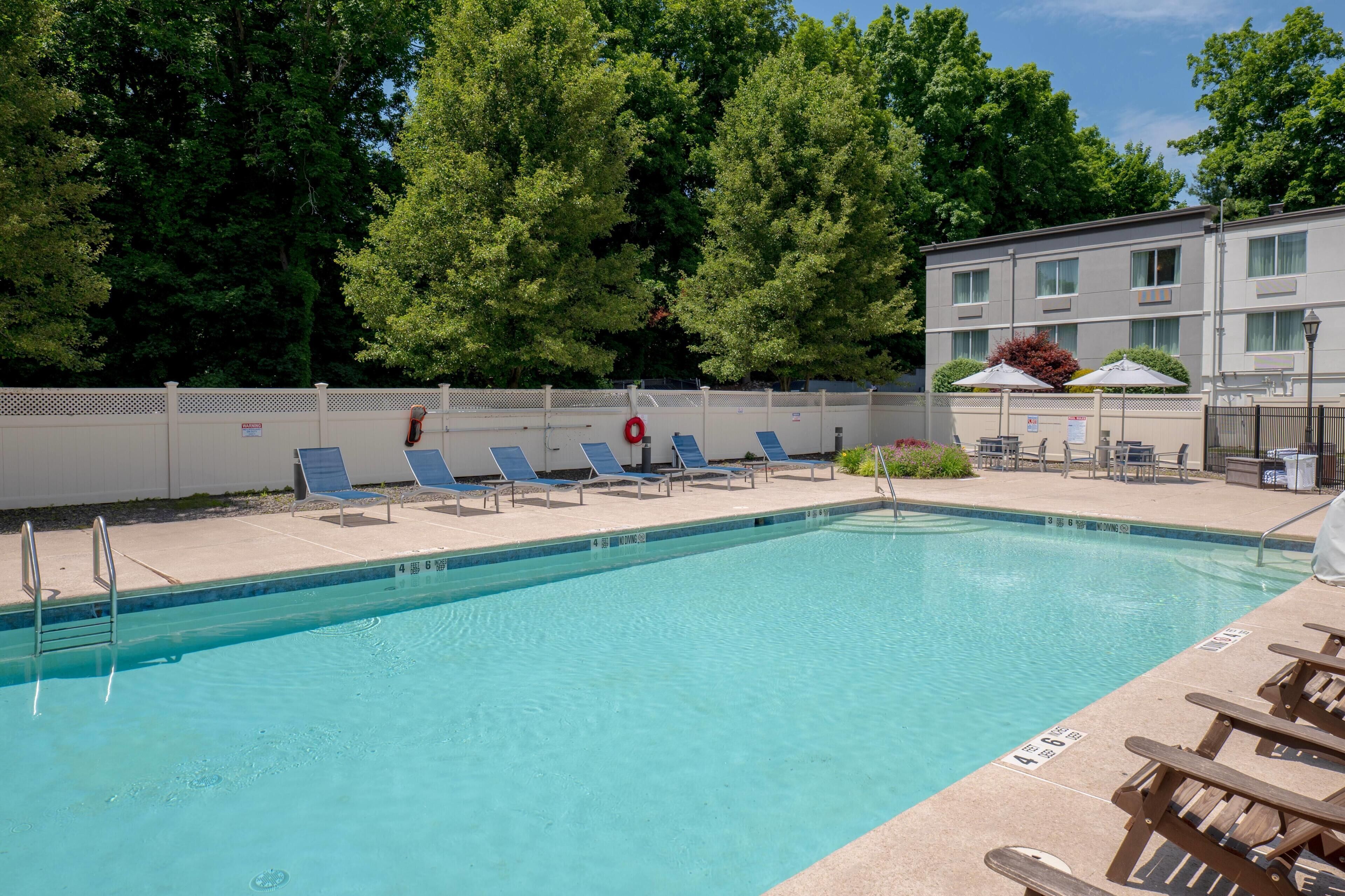 A swimming pool with lounge chairs, a lifebuoy, and a building with a fence in the background.