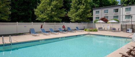 A swimming pool with lounge chairs, a lifebuoy, and a building with a fence in the background.