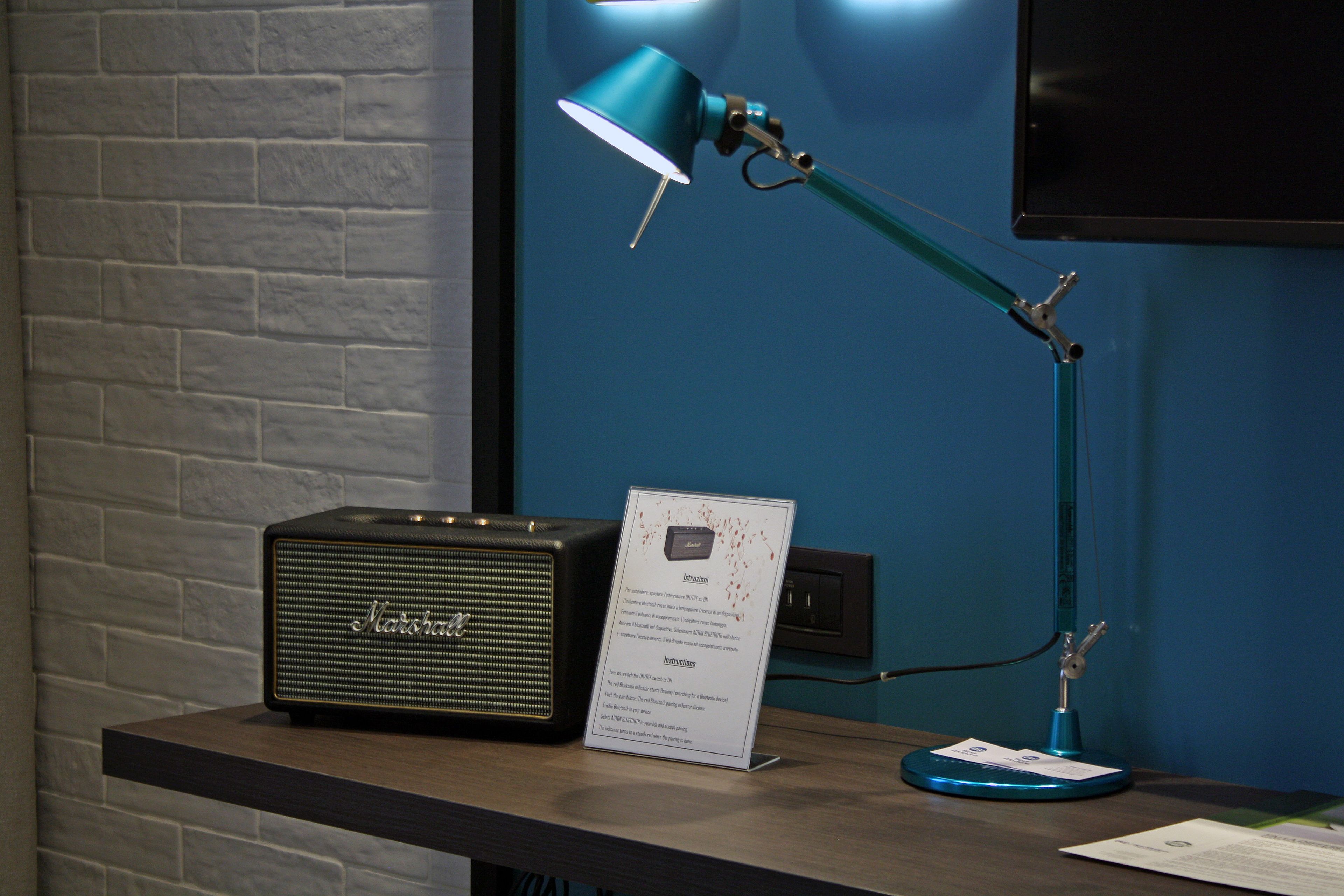 Un bureau agrémenté d’un amplificateur Marshall vintage, d’une lampe de bureau de couleur turquoise et d’un panneau indiquant les consignes.