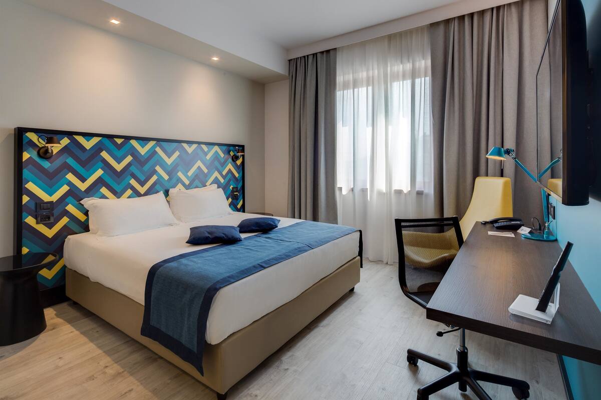 A hotel room with a bed, a desk, a chair, and a TV.