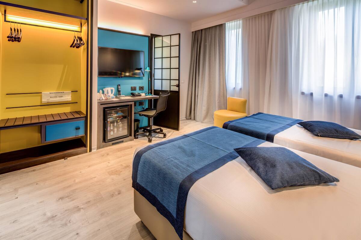 A hotel room with two beds, a desk, a chair, a TV, and a bathroom.
