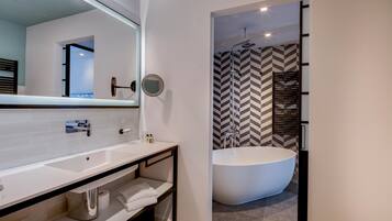 Une salle de bain moderne avec un grand lavabo blanc, un miroir, un miroir rond, une baignoire sur pieds et un mur de douche orné d’un motif en chevrons.