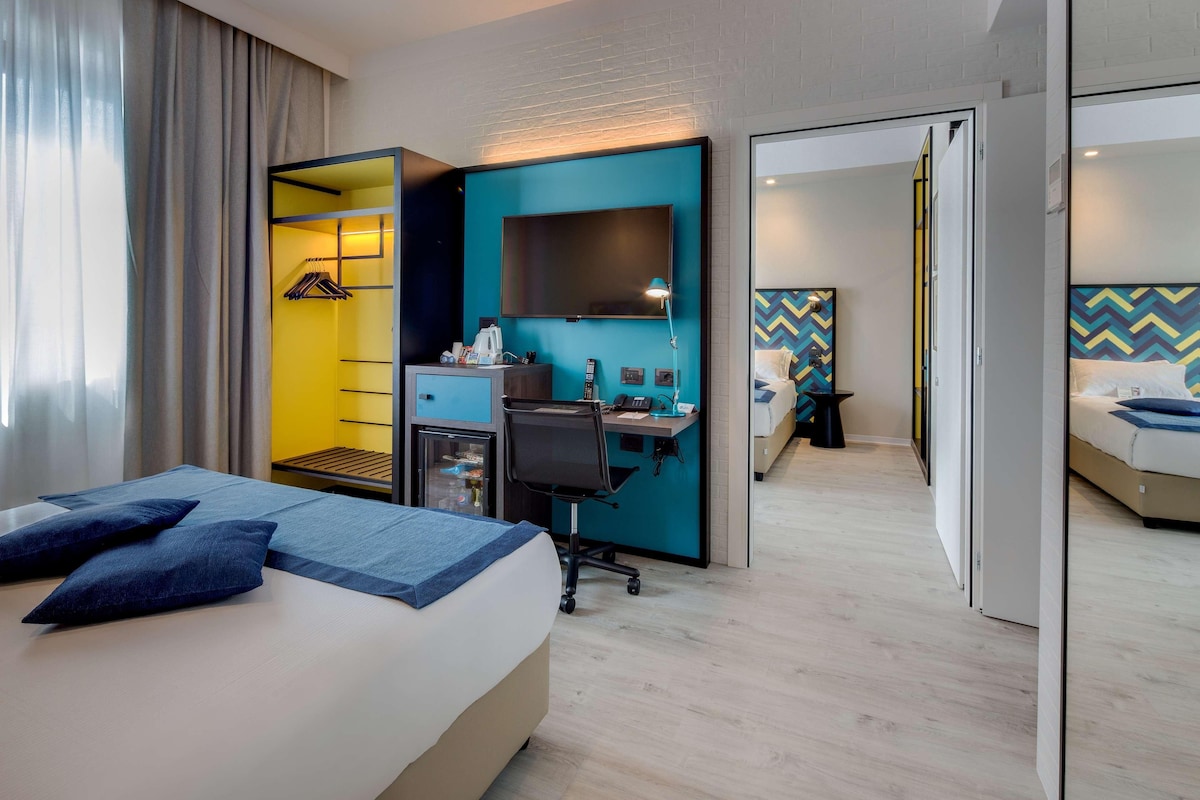 A hotel room with a bed, desk, and a small kitchenette.