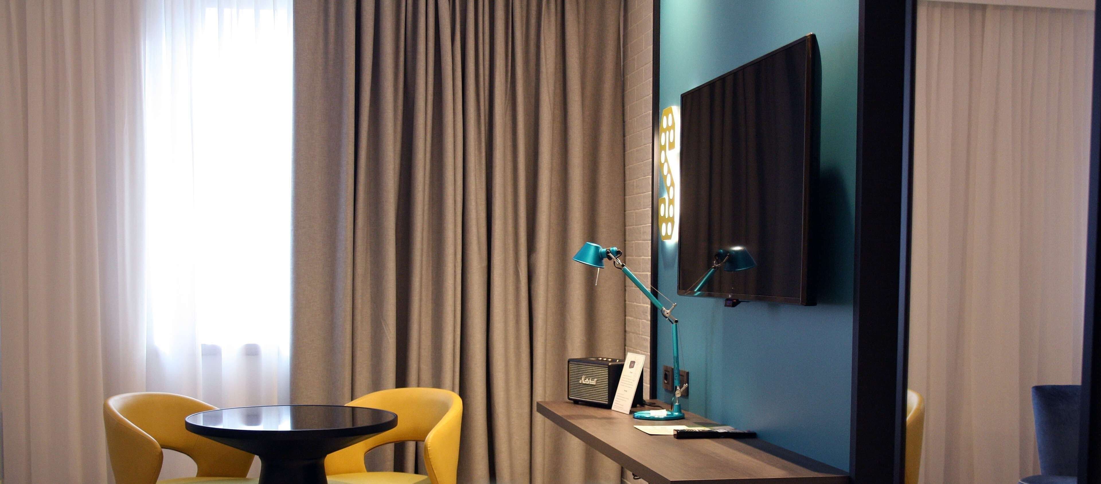 A hotel room with a desk, two chairs, a lamp, a radio, and a mirror.