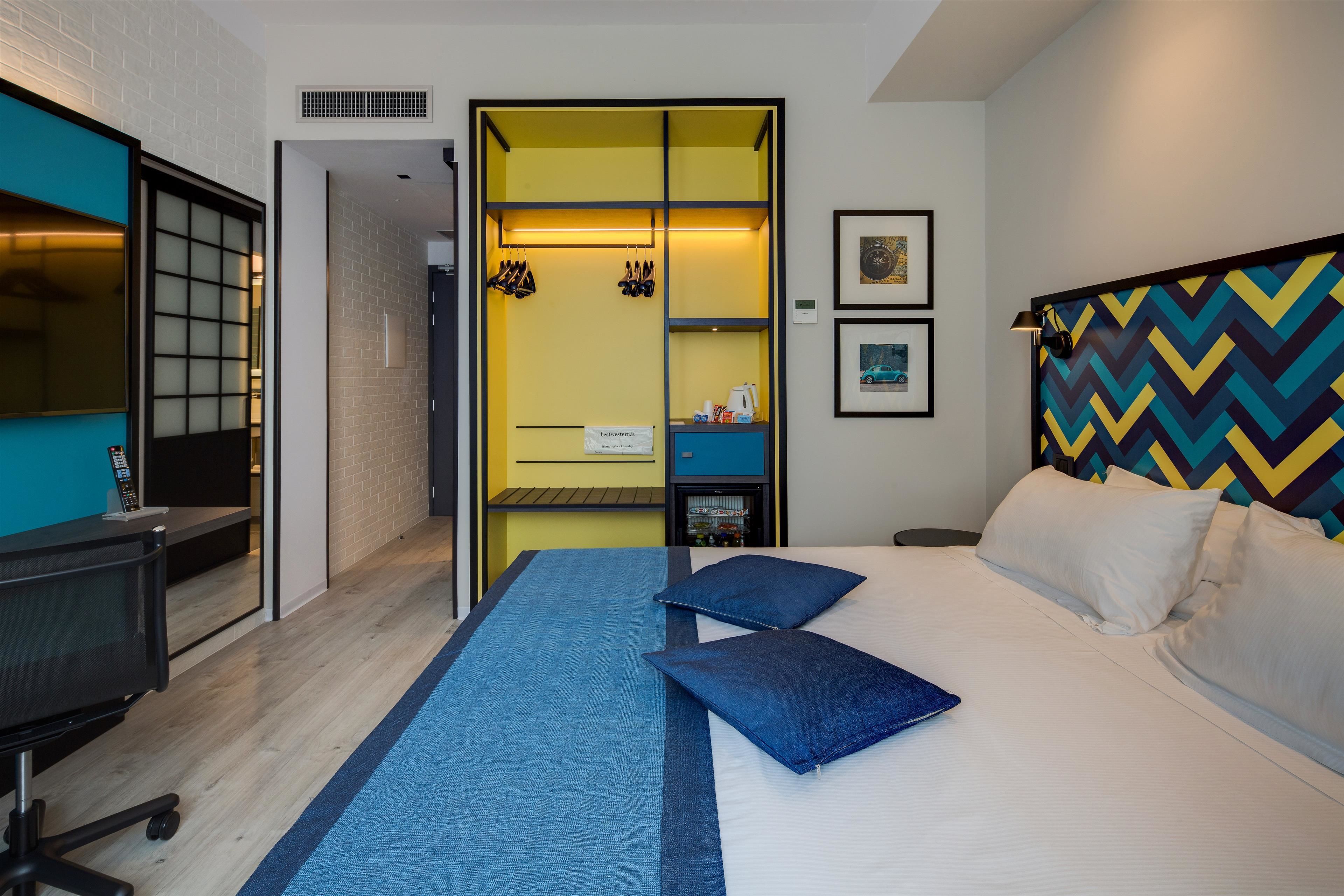 A hotel room with a bed, a desk, a chair, a wardrobe, and a mirror.