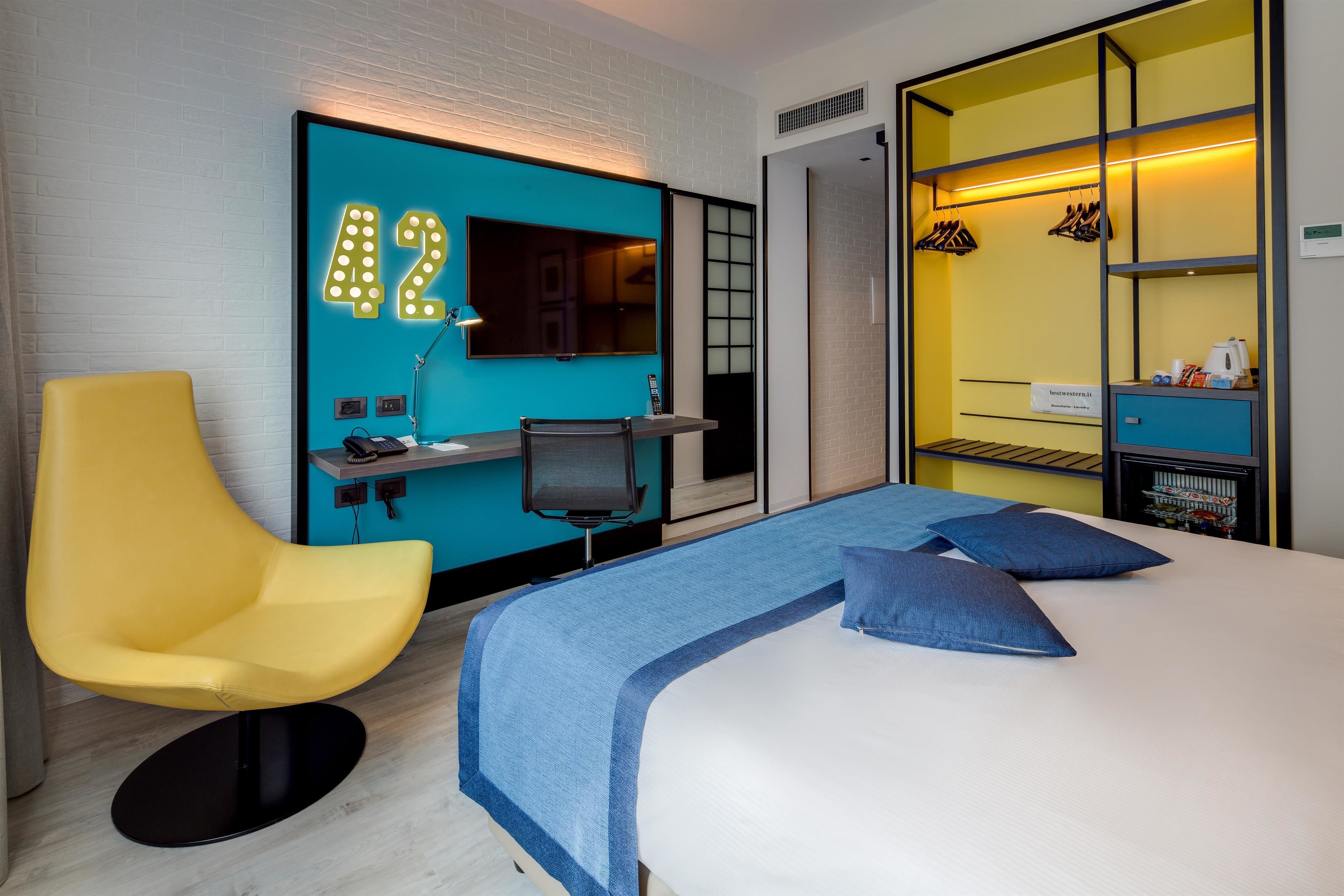 A hotel room with a bed, a desk, a chair, and a wardrobe.