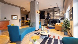 Eine moderne Hotellobby mit einer gebogenen blauen Couch, gelben Stühlen, einem runden Teppich und einem Empfangstresen.