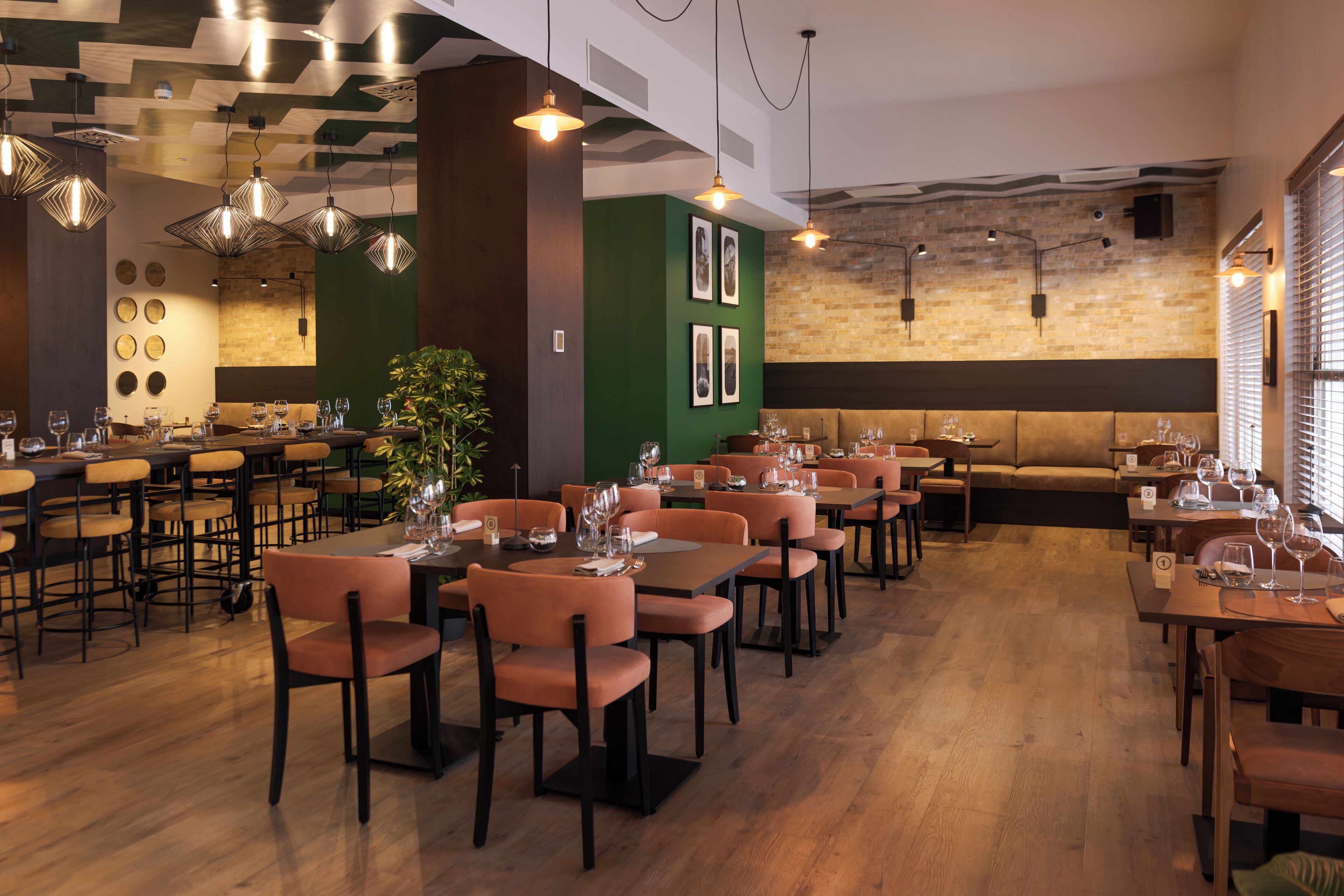 A restaurant with multiple dining tables and chairs, a green accent wall, and hanging pendant lights.