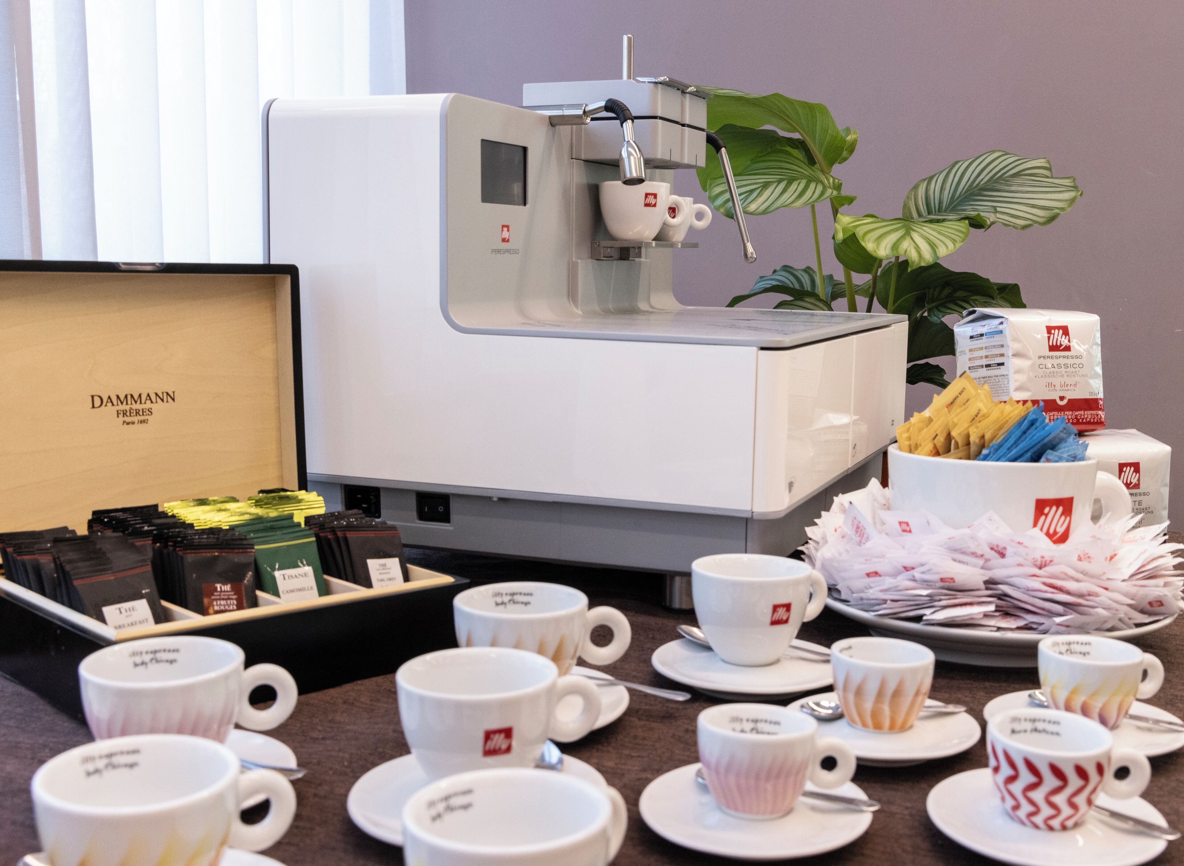 A coffee station with a coffee machine, various coffee pods, and a selection of cups and saucers.
