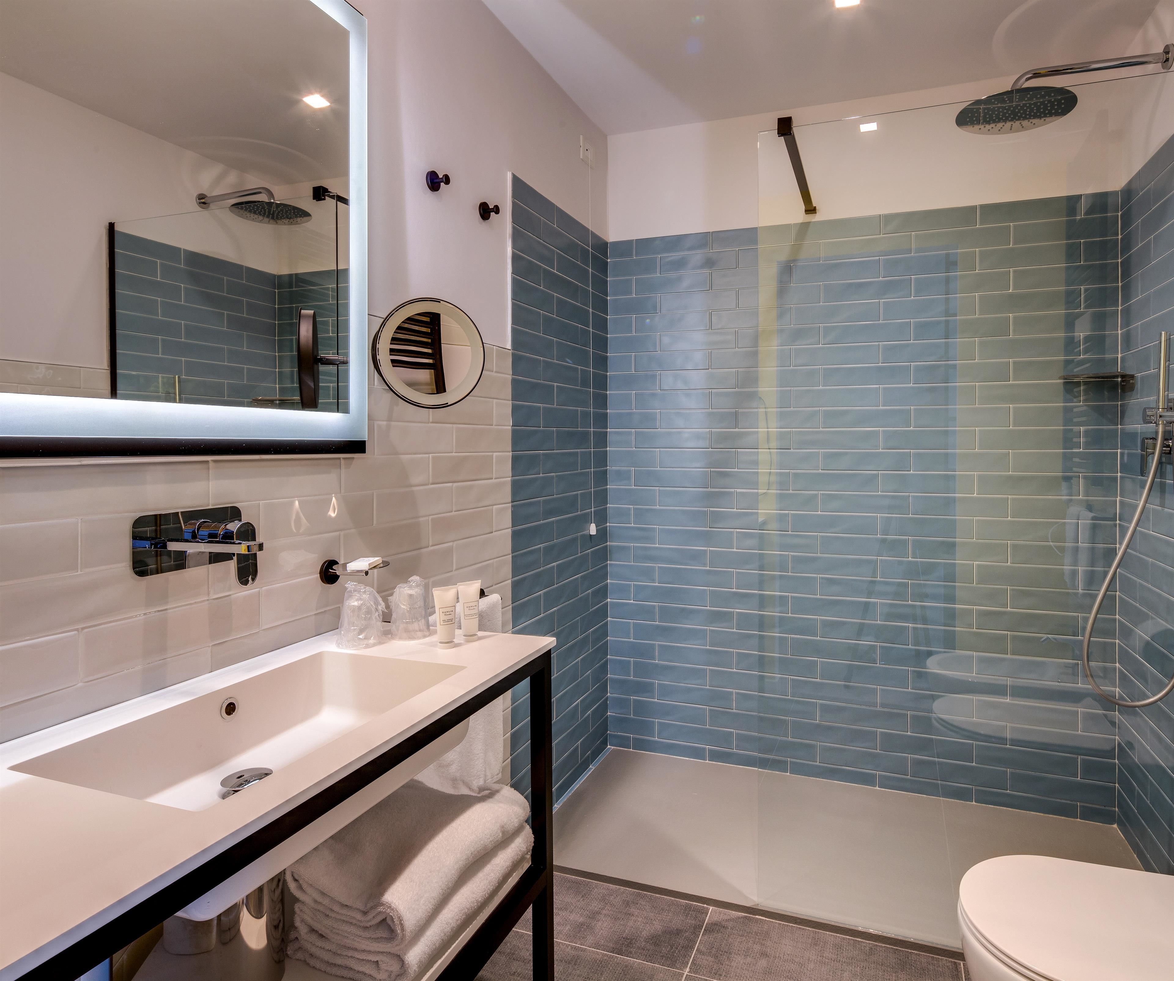 Un baño moderno con lavamanos blanco, espejo y zona de ducha con azulejos azules.