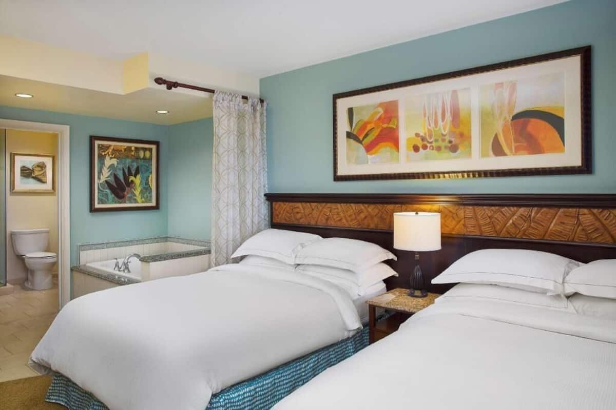 Een hotelkamer met twee bedden, een badkamer en een groot abstract schilderij aan de muur.