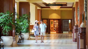 A spacious lobby with a tiled floor, large potted plants, and a couple walking.