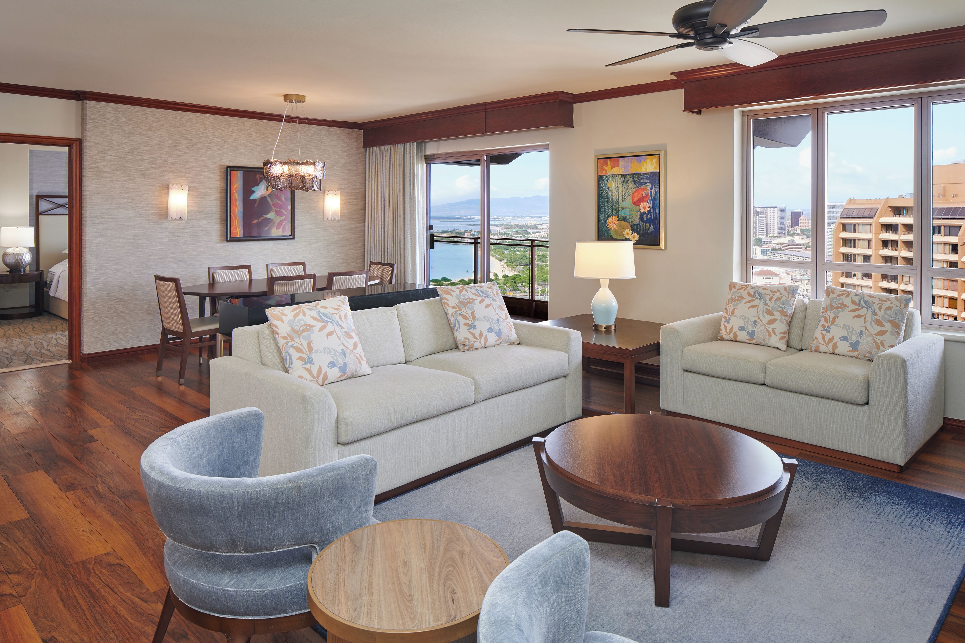 A hotel room with a dining area, two sofas, a coffee table, and a view of the city.