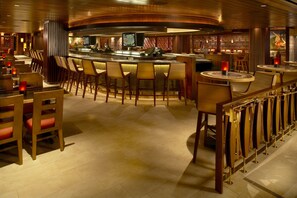 Zona de bar con taburetes de madera, una barra y una pantalla de televisión.
