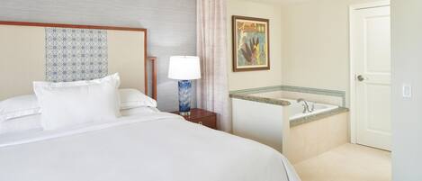A hotel room with a bed, a nightstand with a lamp, a bathroom with a sink and mirror, and a door.