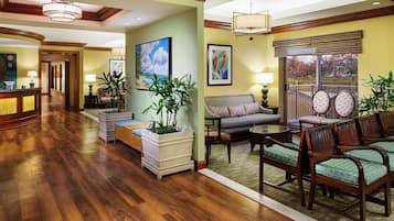 A spacious living area with hardwood flooring, a sofa, a coffee table, and a dining area with chairs. There are potted plants and artwork on the walls.