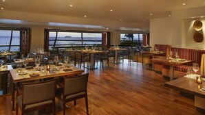 Un vaste espace dédié à la salle à manger, doté d’un plancher en bois, de grandes fenêtres offrant une vue sur l’océan et d’un mobilier moderne.