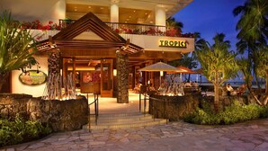 A Tropics restaurant with a stone facade, outdoor seating, and a view of the ocean. - Hilton Grand Vacations Club Grand Waikikian Honolulu (Honolulu)