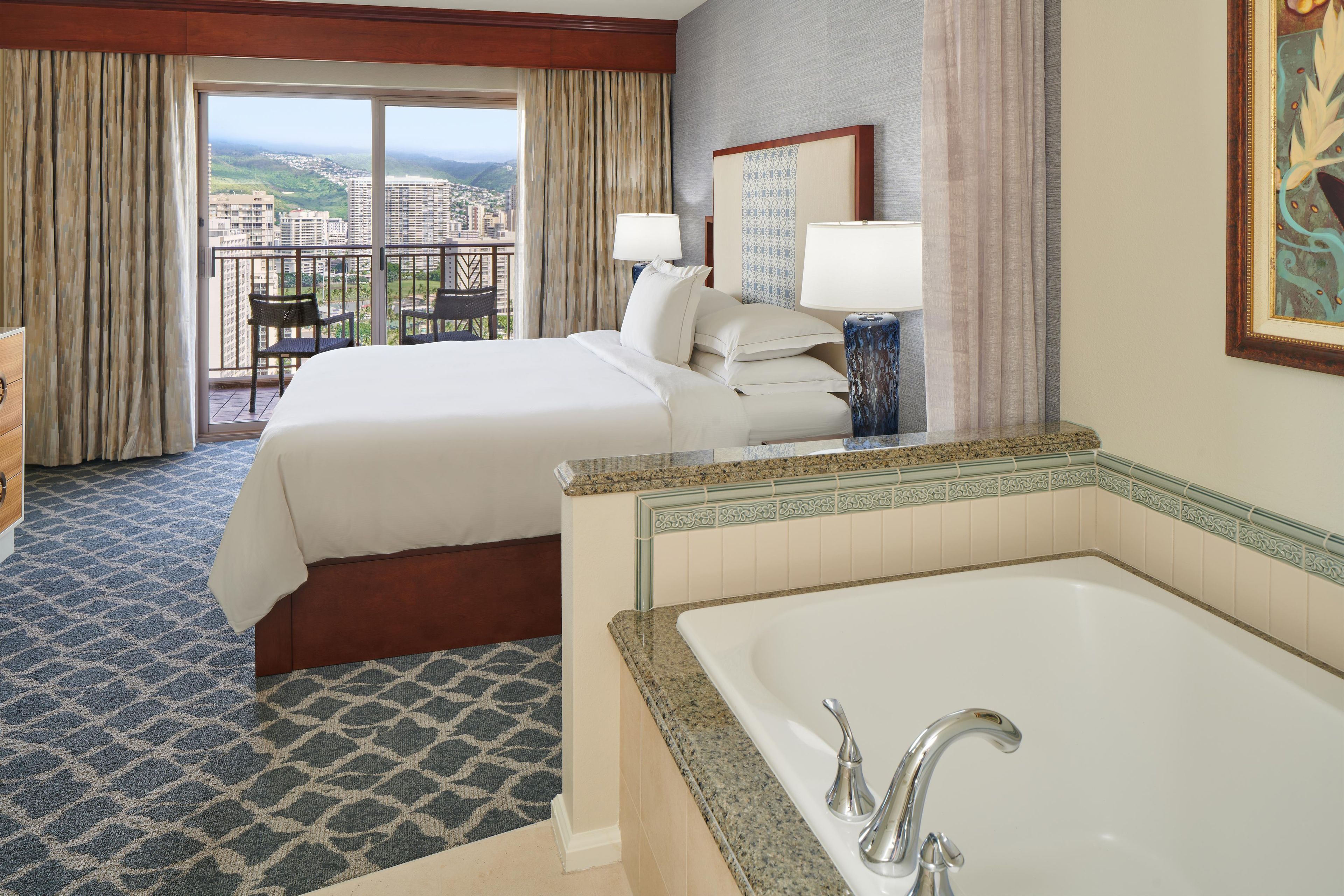 Habitación de hotel con cama, baño con bañera y balcón con vistas a la ciudad.