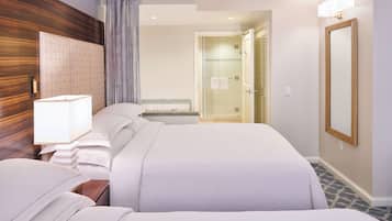 A hotel room with a large bed, a bedside table with a lamp, a mirror, and a shower area.