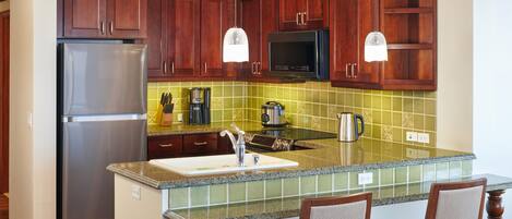 A kitchen with wooden cabinets, a stainless steel refrigerator, a microwave, and a granite countertop.