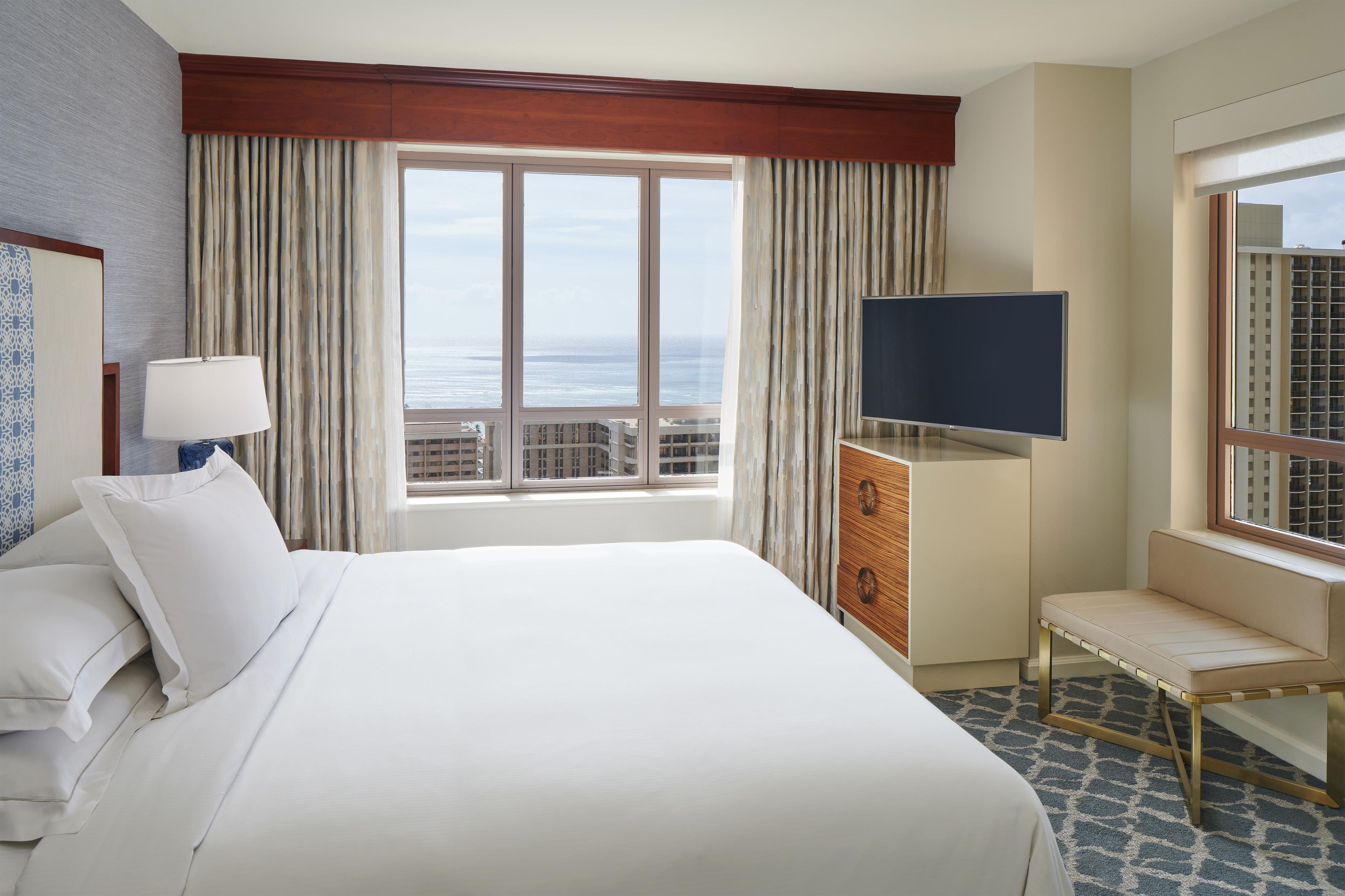 A hotel room with a large bed, a TV, a seating area, and a view of the ocean.