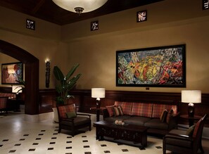 Een hal met een groot abstract schilderij, een potplant en een zithoek met een gestreept sofa en fauteuils.