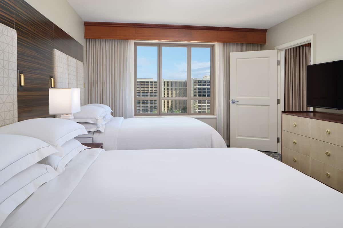 Hotelkamer met twee bedden, een televisie, een dressoir en een groot raam met uitzicht op de stad.