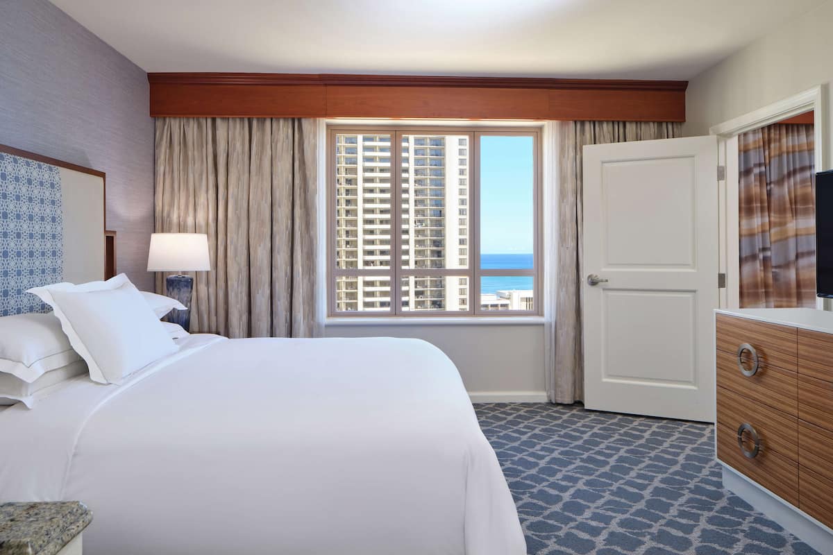 Een hotelkamer met een groot bed, een kaptafel, een raam met uitzicht op gebouwen en een deur.