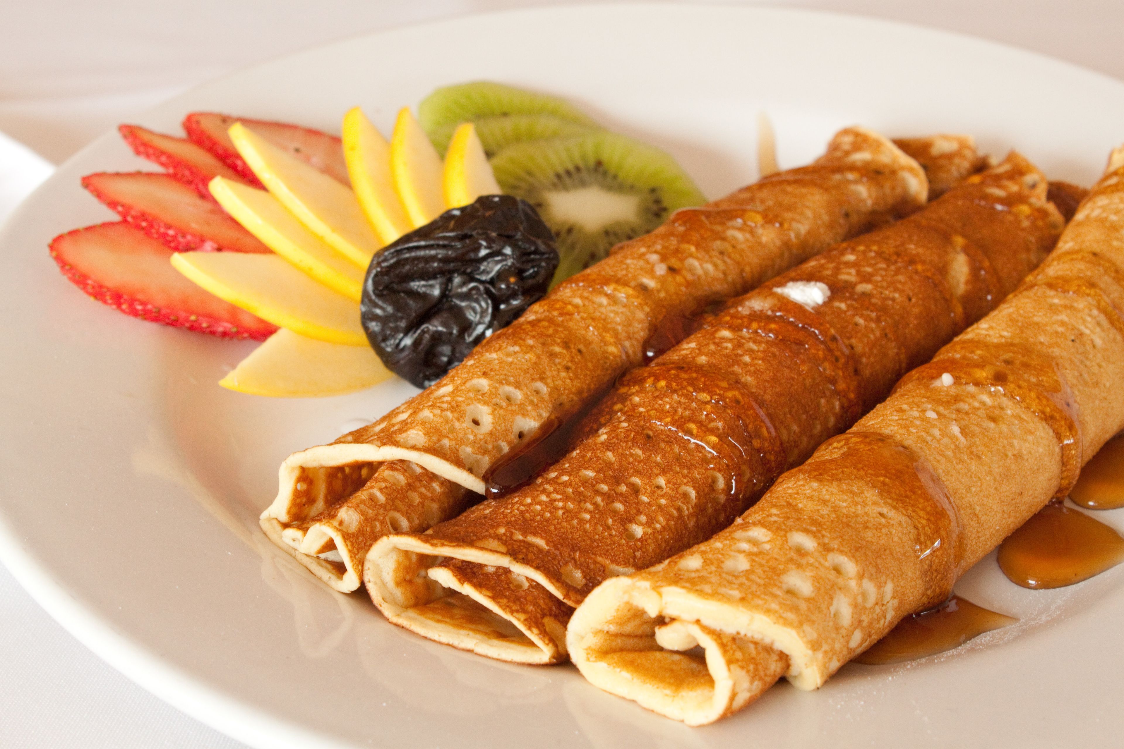 Un plato con tres tortitas enrolladas, fresas en rodajas, kiwi y un dátil.