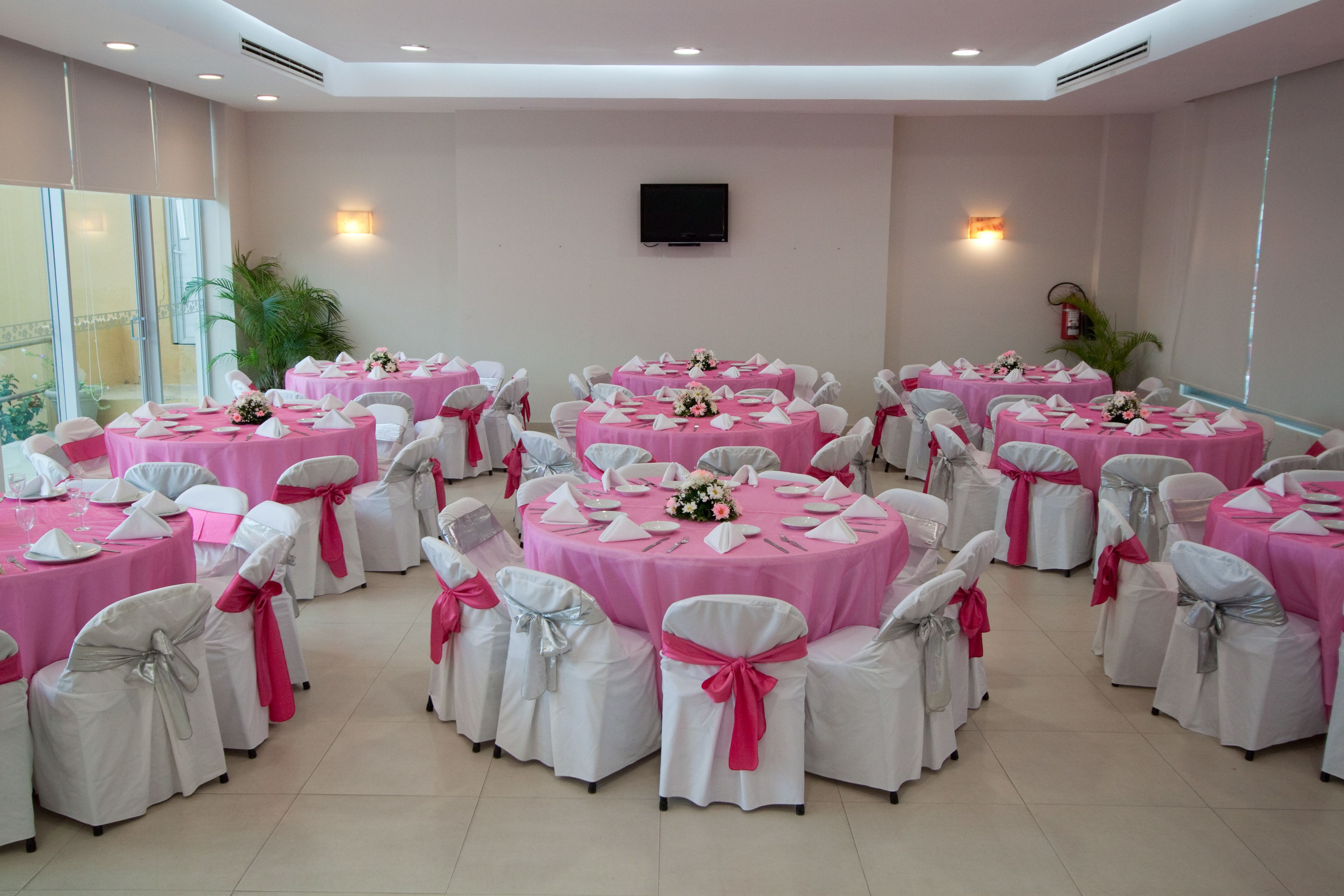A conference room with multiple round tables, each covered with a pink tablecloth and white chairs with pink sashes.
