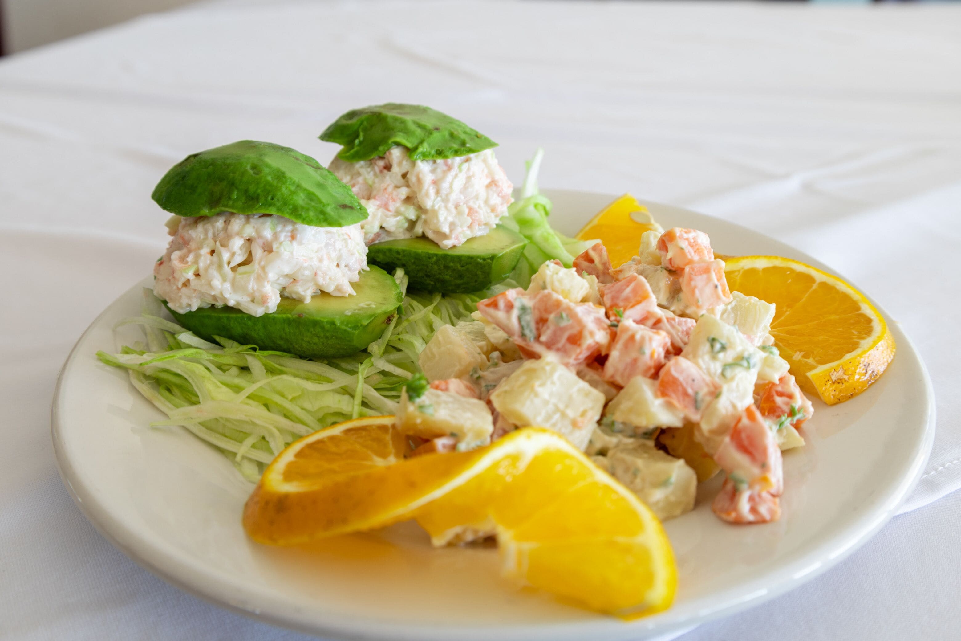 A plate of food with avocado slices, salmon salad, and orange slices.