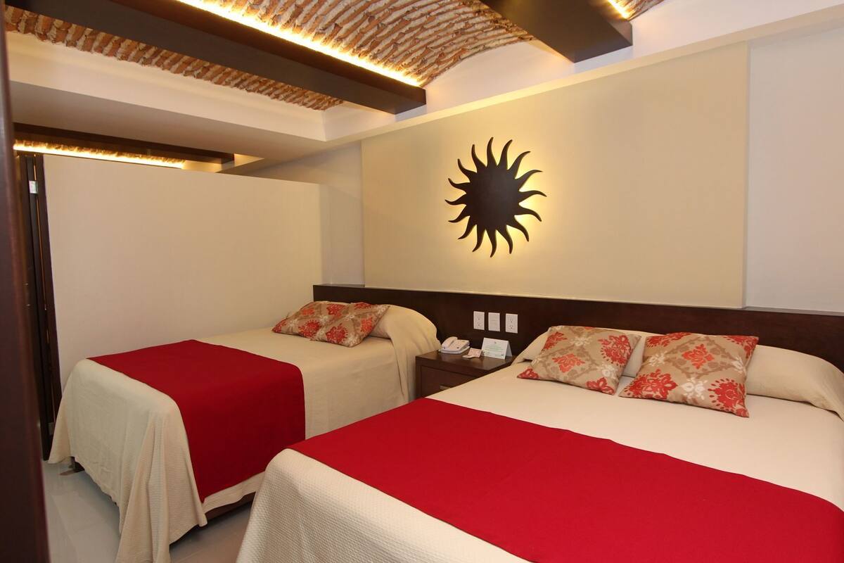 Ein Hotelzimmer mit zwei Betten, einer Wanddekoration in Sonnenform und einer Holzbalkendecke.
