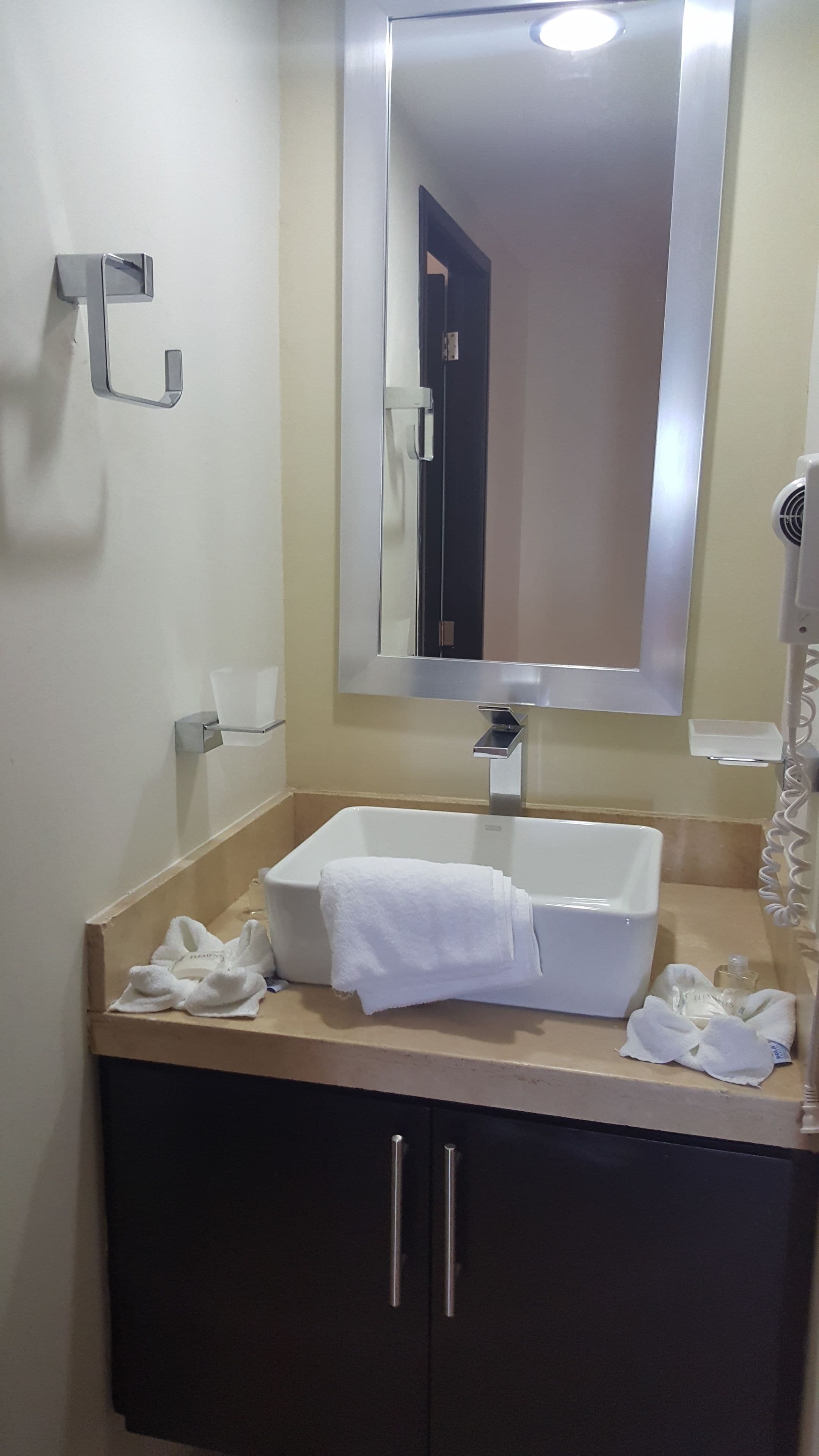 Un baño con un lavamanos blanco, un espejo y un perchero para toallas.