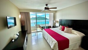 Habitación de hotel con cama, televisión, escritorio, lámpara y vista al mar.