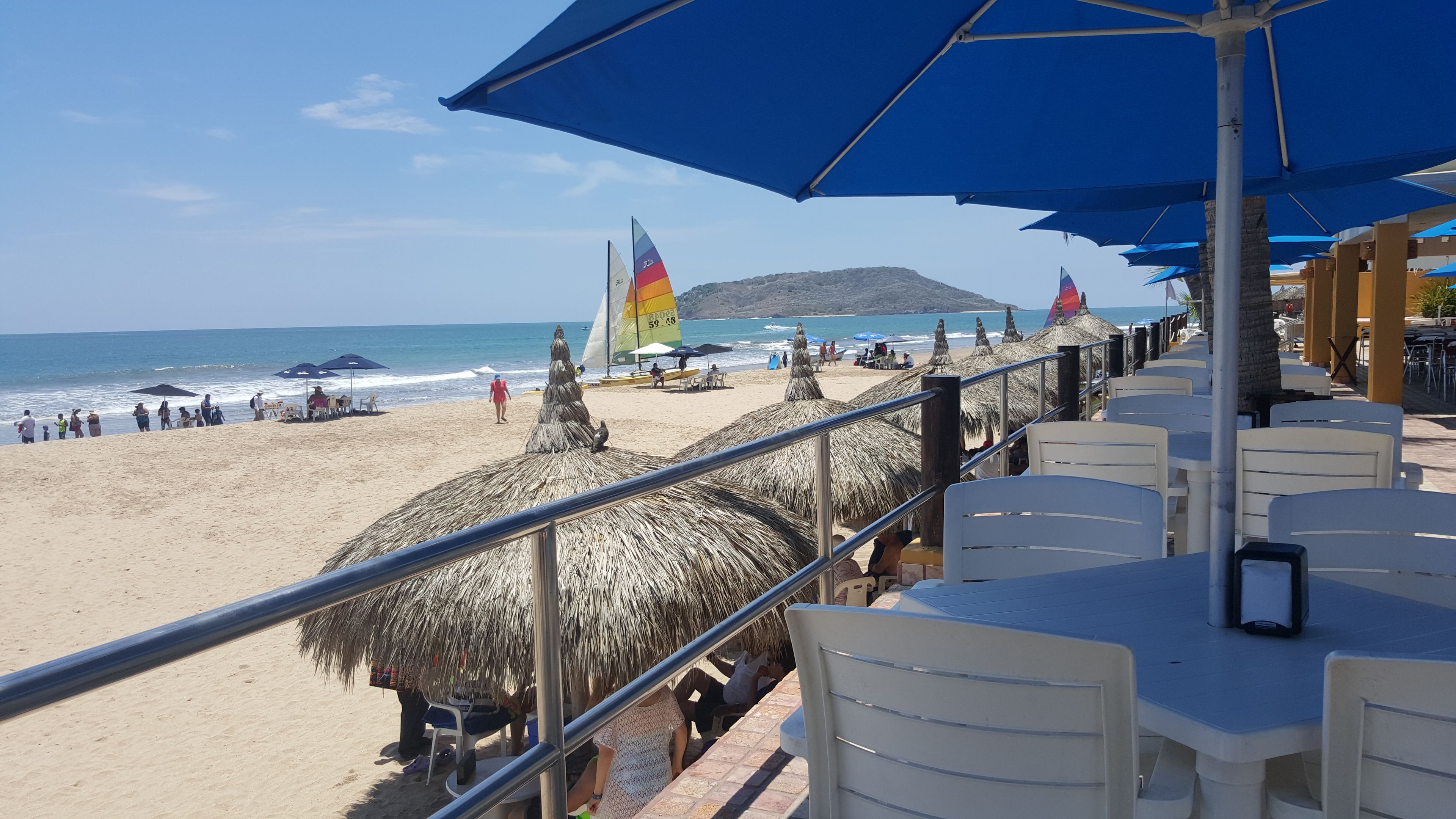 A beachside restaurant with thatched umbrellas, white plastic chairs, and a view of the ocean.