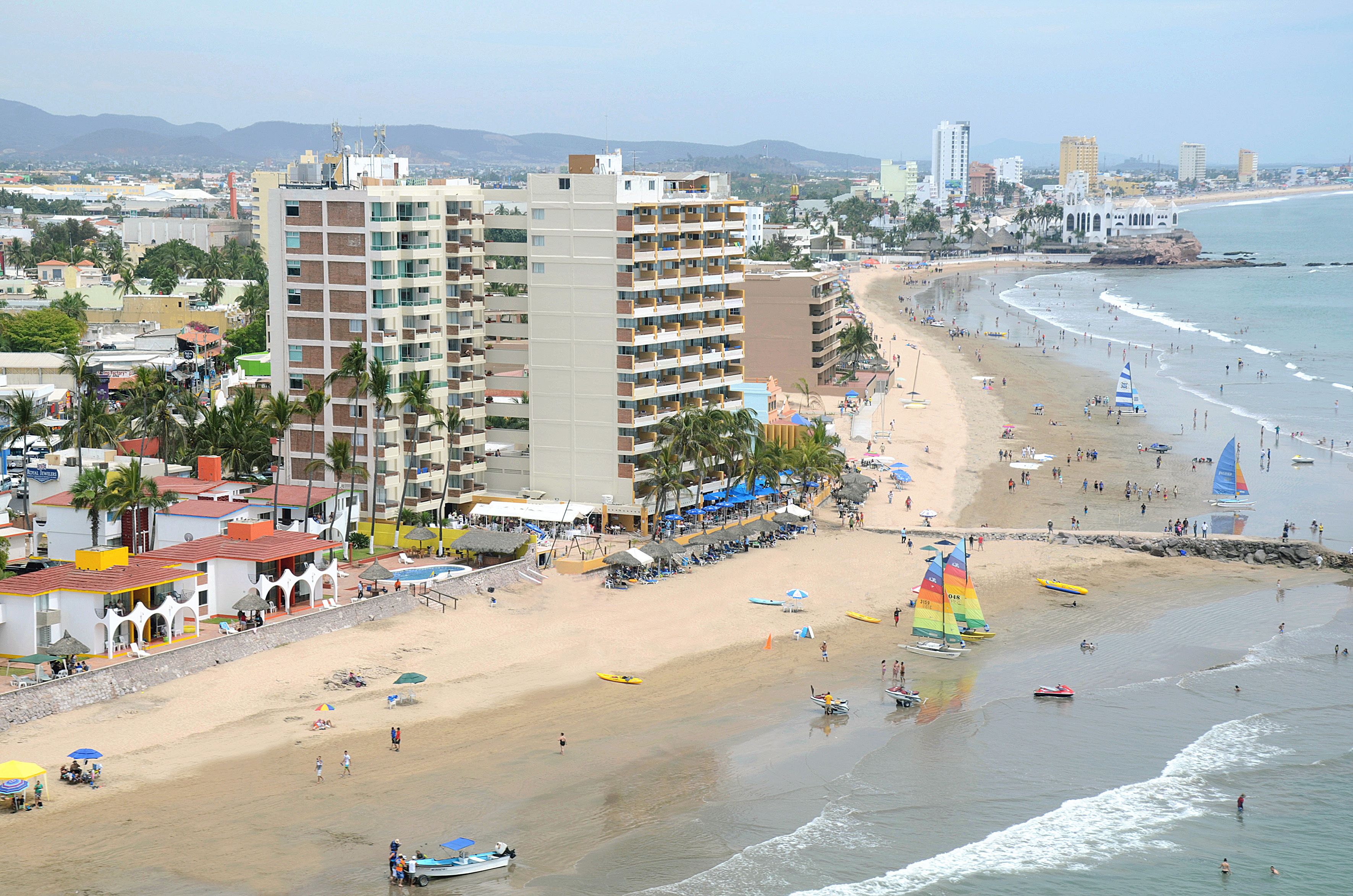 A beachside hotel with multiple floors, a sandy beach, and a view of the ocean.