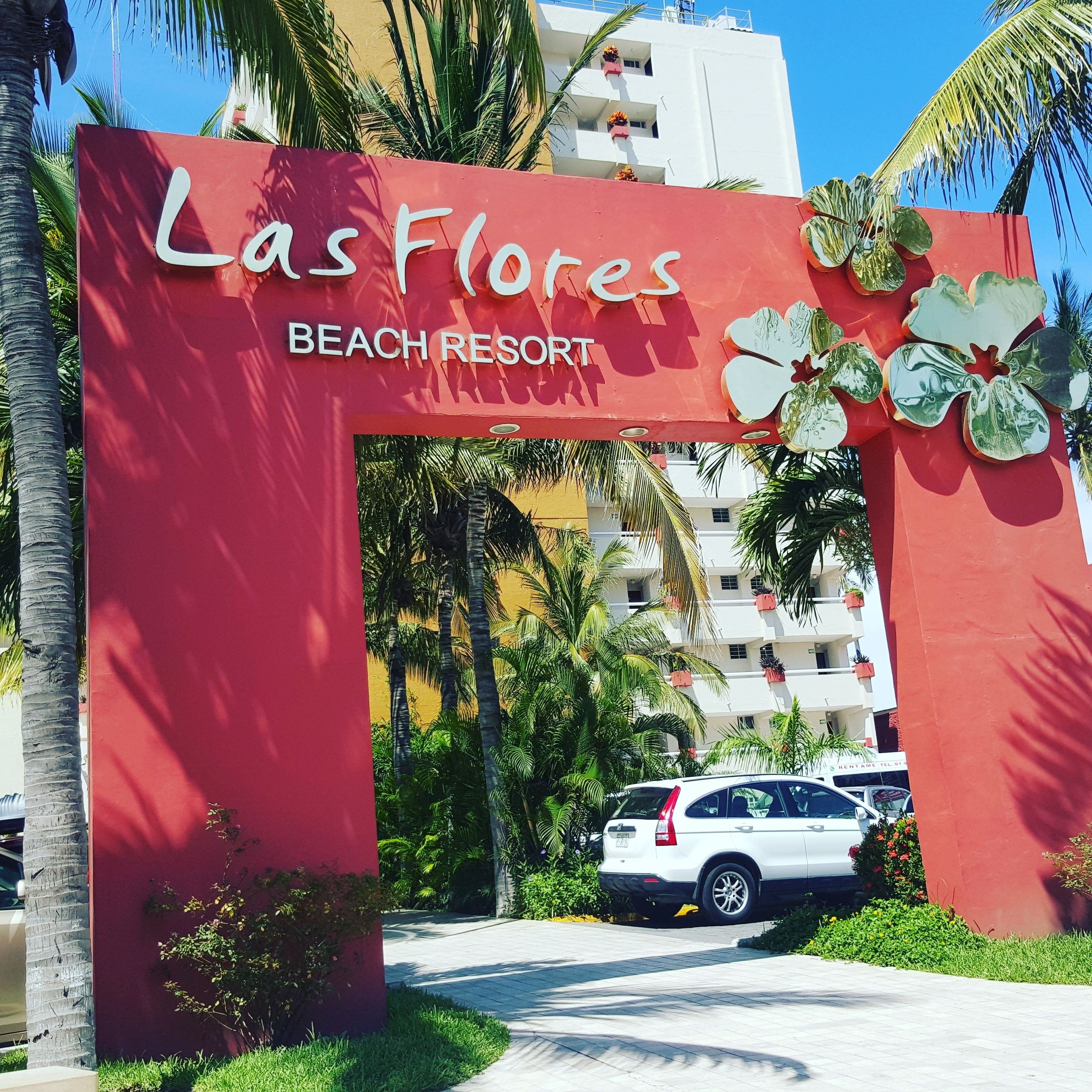 A red archway with the text "Las Flores Beach Resort" and decorative flowers.