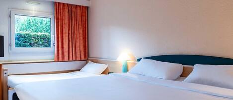 A hotel room with a bed, a window with curtains, a nightstand, and a lamp.