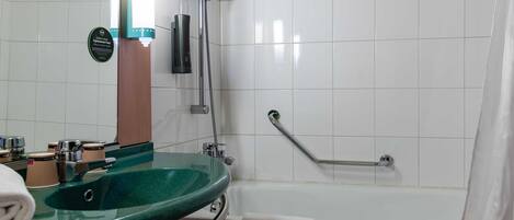 A bathroom with a green sink, a white bathtub, and a shower with a grab bar.