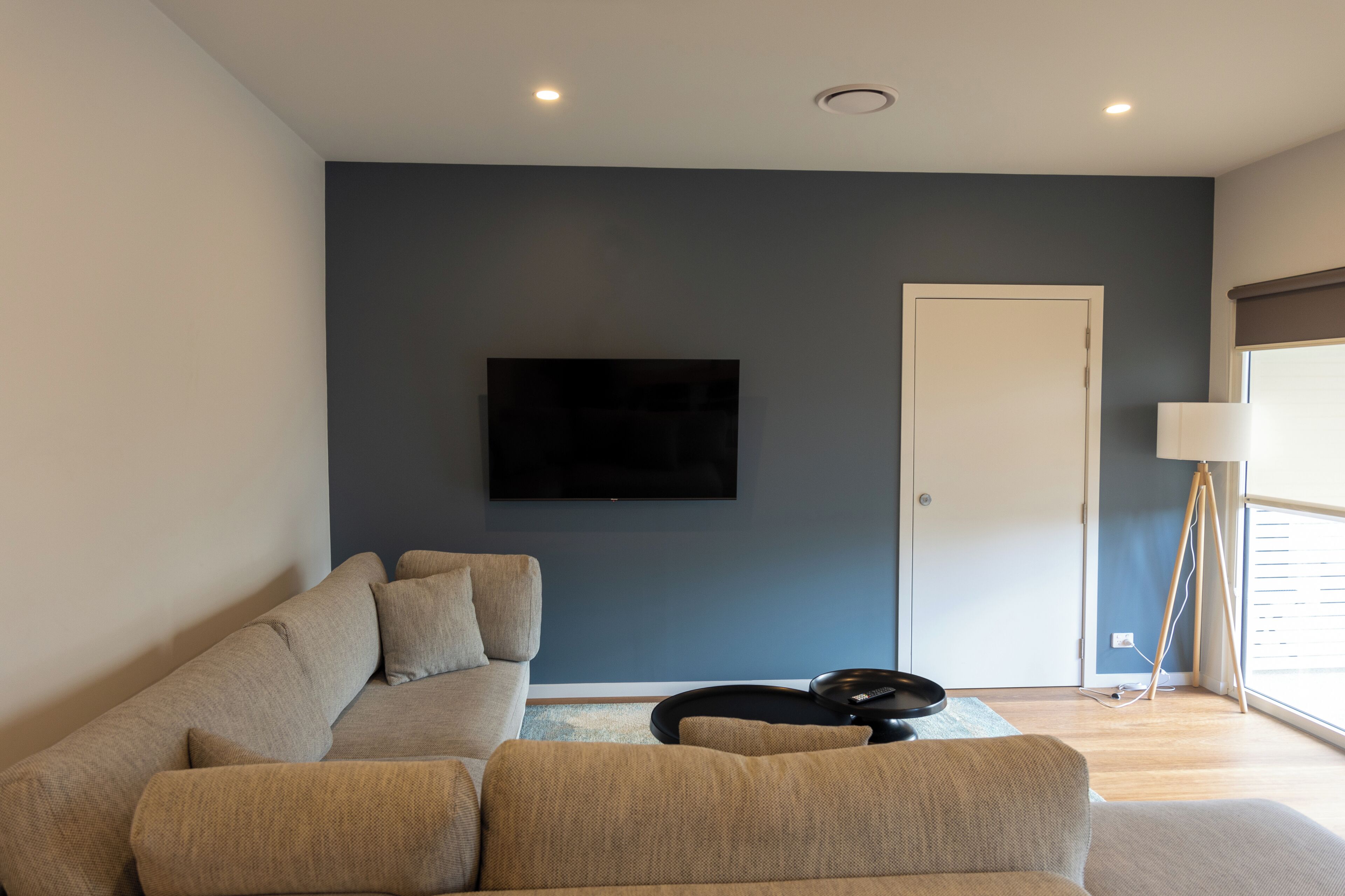 A modern living room with a sofa, a flat-screen TV mounted on the wall, and a floor lamp.