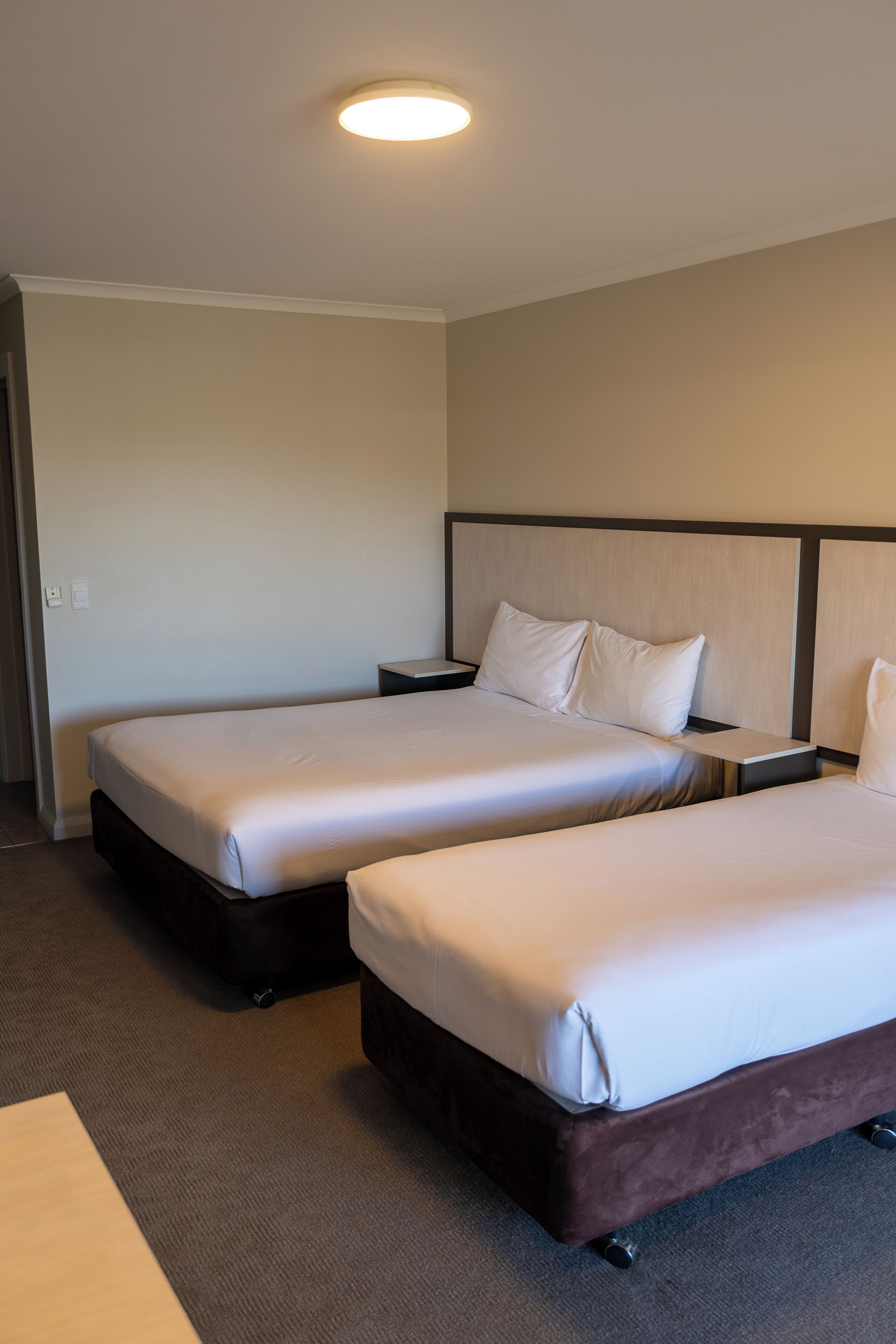 A hotel room with two beds, a carpeted floor, and a ceiling light.