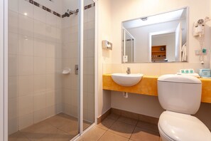 A bathroom with a glass-enclosed shower, a sink with a yellow countertop, a white toilet, and a mirror above the sink.