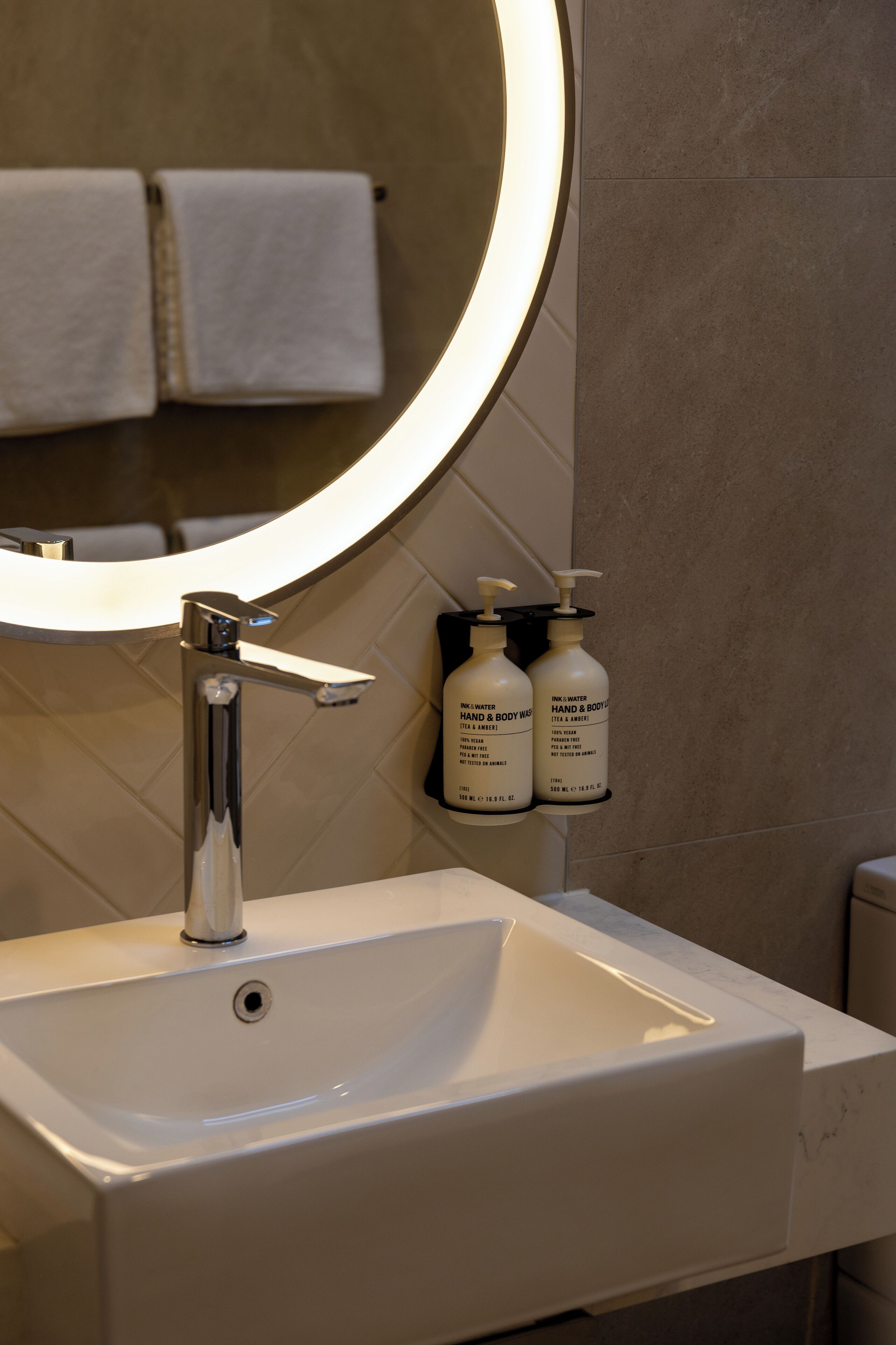 A bathroom with a white sink, a mirror with a light, and two bottles of hand and body wash.