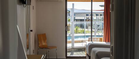 Ett hotellrum med ett skrivbord, två sängar, en stol och utsikt över en pool.