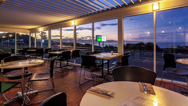 An indoor dining area with tables and chairs, large windows, and a view of the sky. - Beachfront At Bicheno (Bicheno)