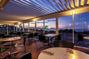 Un comedor interior con mesas y sillas, ventanas amplias y vista al cielo.