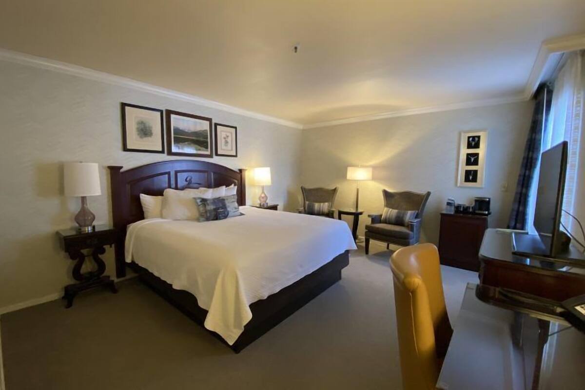 A hotel room with a large bed, bedside tables with lamps, a desk with a chair, and a television.