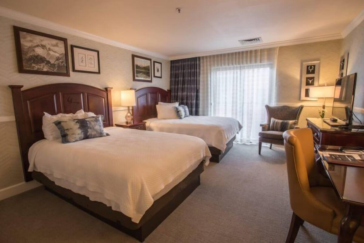 A hotel room with two beds, a desk, a chair, and a television.